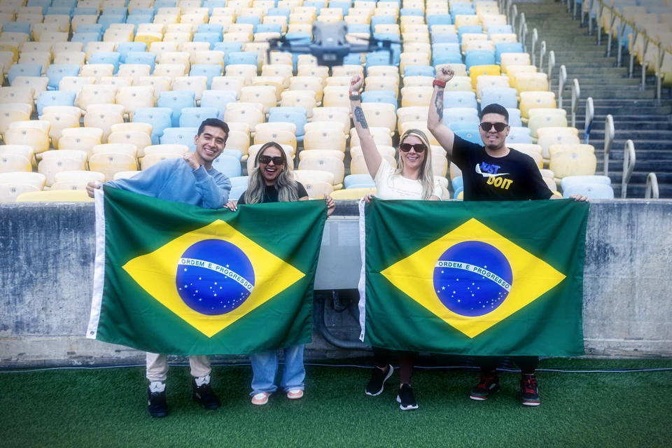 Visitantes com bandeiras do Brasil no gramado do Maracanã enquanto um drone os filma.